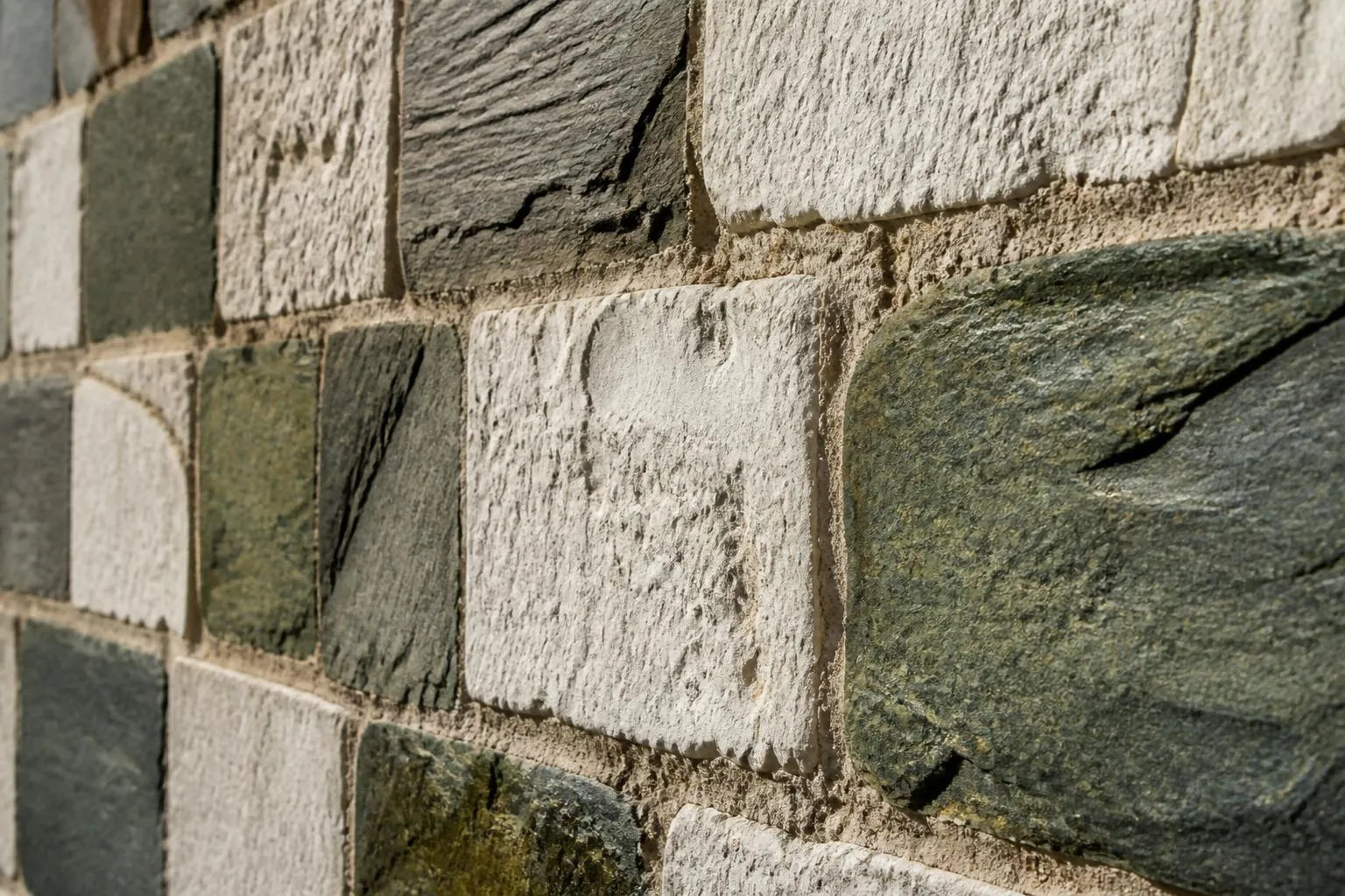 gros plan sur l'appareil de pierre d'un mur d'église romane, blocs de serpentine vert sombre et de calcaire blanc alternés en damier irrégulier, joints de mortier visibles, lumière rasante